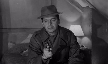 Movie still from “Le Doulos” (1962), directed by Jean-Pierre Melville – A black and white photo of a man holding a gun; Medium shot, Low angle