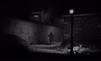 Movie still from “Le Doulos” (1962), directed by Jean-Pierre Melville – A person walking down a street at night; Wide shot, Over the shoulder angle