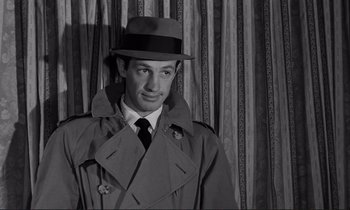 Movie still from “Le Doulos” (1962), directed by Jean-Pierre Melville – A black and white photo of a man wearing a hat and coat; Close Up shot, Over the shoulder angle