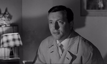 Movie still from “Le Doulos” (1962), directed by Jean-Pierre Melville – Black and white photograph of a man wearing a suit and tie; Close Up shot, Low angle