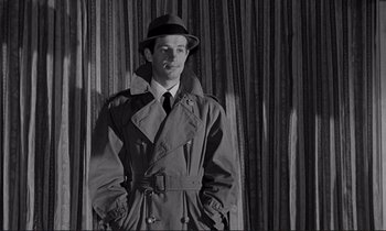 Movie still from “Le Doulos” (1962), directed by Jean-Pierre Melville – A man wearing a trench coat and hat; Medium shot, Low angle