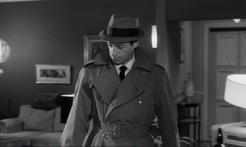 Movie still from “Le Doulos” (1962), directed by Jean-Pierre Melville – A man wearing a hat and a trench coat; Medium shot, Over the shoulder angle