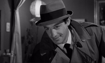 Movie still from “Le Doulos” (1962), directed by Jean-Pierre Melville – A black and white photo of a man wearing a hat; Close Up shot, Over the shoulder angle