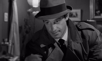 Movie still from “Le Doulos” (1962), directed by Jean-Pierre Melville – A black and white photo of a man wearing a hat; Close Up shot, Over the shoulder angle