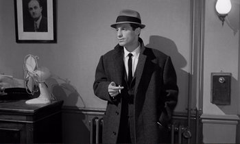 Movie still from “Le Doulos” (1962), directed by Jean-Pierre Melville – A black and white photo of a man smoking a cigarette; Medium shot, Low angle