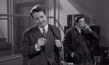 Movie still from “Le Doulos” (1962), directed by Jean-Pierre Melville – A man in a suit and tie standing next to another man in a suit and tie; Medium shot, Over the shoulder angle