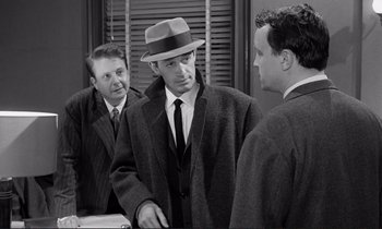 Movie still from “Le Doulos” (1962), directed by Jean-Pierre Melville – A man in a hat is talking to two other men; Medium shot, Over the shoulder angle