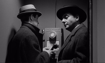 Movie still from “Le Doulos” (1962), directed by Jean-Pierre Melville – Two men in suits and hats are looking at each other; Close Up shot, Low angle