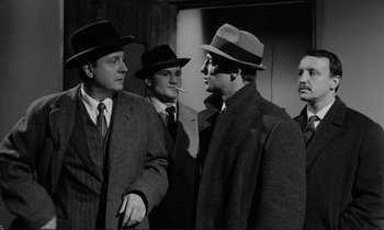 Movie still from “Le Doulos” (1962), directed by Jean-Pierre Melville – A black and white photo of a group of men talking; Medium shot, Low angle