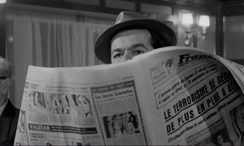 Movie still from “Le Doulos” (1962), directed by Jean-Pierre Melville – A man in a hat is reading a newspaper; Close Up shot, Low angle