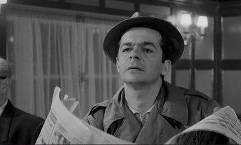 Movie still from “Le Doulos” (1962), directed by Jean-Pierre Melville – A black and white photo of a man reading a newspaper; Close Up shot, Low angle