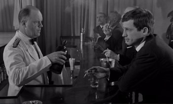 Movie still from “Le Doulos” (1962), directed by Jean-Pierre Melville – A black and white photo of men sitting at a bar; Medium shot, Over the shoulder angle