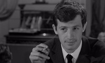 Movie still from “Le Doulos” (1962), directed by Jean-Pierre Melville – A man in a suit and tie smoking a cigarette; Close Up shot, High angle