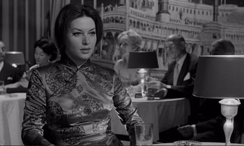 Movie still from “Le Doulos” (1962), directed by Jean-Pierre Melville – A black and white photo of a woman sitting at a table; Medium shot, Low angle