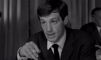 Movie still from “Le Doulos” (1962), directed by Jean-Pierre Melville – A black and white photo of a man smoking a cigarette; Close Up shot, Low angle