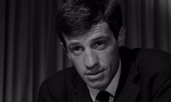 Movie still from “Le Doulos” (1962), directed by Jean-Pierre Melville – Black and white photograph of a man wearing a suit; Close Up shot, Low angle