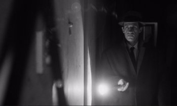 Movie still from “Le Doulos” (1962), directed by Jean-Pierre Melville – A black and white photo of a man holding a flashlight; Medium shot, Low angle