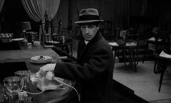 Movie still from “Le Doulos” (1962), directed by Jean-Pierre Melville – A black and white photo of a man in a suit and hat; Medium shot, High angle