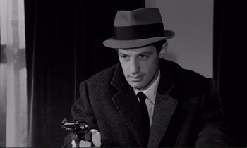 Movie still from “Le Doulos” (1962), directed by Jean-Pierre Melville – A black and white photo of a man holding a gun; Close Up shot, Over the shoulder angle