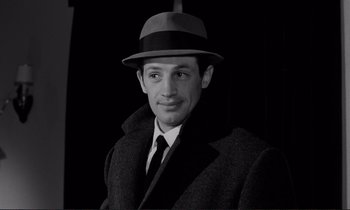 Movie still from “Le Doulos” (1962), directed by Jean-Pierre Melville – A black and white photo of a man wearing a hat and a coat; Close Up shot, Over the shoulder angle