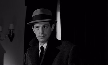 Movie still from “Le Doulos” (1962), directed by Jean-Pierre Melville – A black and white photo of a man wearing a hat and a coat; Close Up shot, Low angle