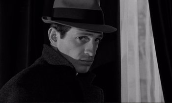 Movie still from “Le Doulos” (1962), directed by Jean-Pierre Melville – A black and white photo of a man wearing a hat; Close Up shot, Low angle