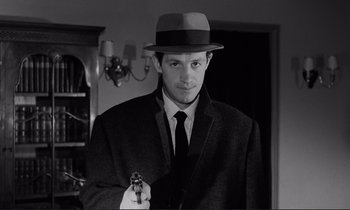 Movie still from “Le Doulos” (1962), directed by Jean-Pierre Melville – A man holding a gun in a room; Close Up shot, Low angle