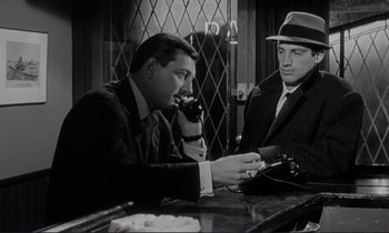 Movie still from “Le Doulos” (1962), directed by Jean-Pierre Melville – Two men in suits and hats sitting at a bar; Medium shot, Low angle