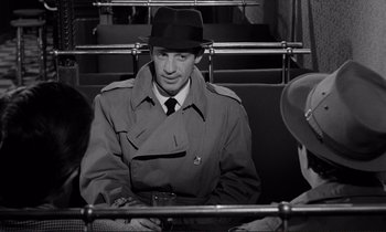 Movie still from “Le Doulos” (1962), directed by Jean-Pierre Melville – A black and white photo of a man in a trench coat and a hat; Close Up shot, Over the shoulder angle