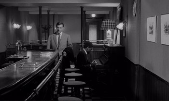 Movie still from “Le Doulos” (1962), directed by Jean-Pierre Melville – Two men are sitting at a bar and one of them is playing the piano; Wide shot, High angle
