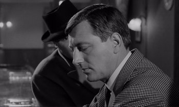 Movie still from “Le Doulos” (1962), directed by Jean-Pierre Melville – A black and white photo of a man in a suit and a hat; Close Up shot, Over the shoulder angle