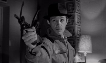 Movie still from “Le Doulos” (1962), directed by Jean-Pierre Melville – A man in a hat holding a gun in his hand; Close Up shot, Low angle