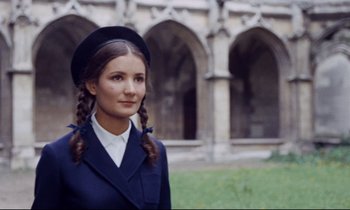 Movie still from “Le Grand Amour” (1969), directed by Pierre Étaix – A young woman in a blue suit and a hat with plaits in front of an old building; Close Up shot, Low angle