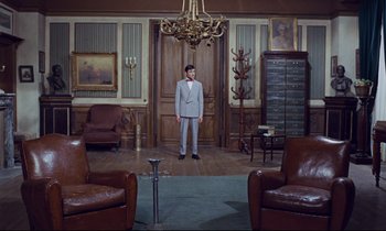 Movie still from “Le Grand Amour” (1969), directed by Pierre Étaix – A man in a suit standing in a living room; Wide shot, High angle