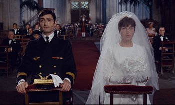 Movie still from “Le Grand Amour” (1969), directed by Pierre Étaix – A man and a woman sitting in front of each other in a church; Medium shot, Low angle