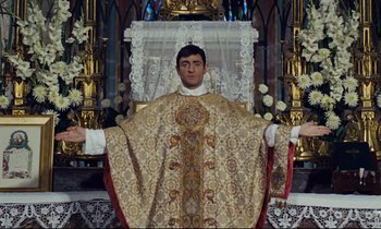 Movie still from “Le Grand Amour” (1969), directed by Pierre Étaix – A man wearing a priest's outfit standing in front of a chair; Medium shot, Low angle