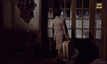 Movie still from “Le Grand Amour” (1969), directed by Pierre Étaix – A woman with a suitcase walking into a room; Wide shot, High angle