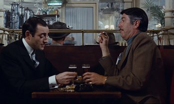 Movie still from “Le Grand Amour” (1969), directed by Pierre Étaix – Two men sitting at a table in front of each other; Medium shot, Over the shoulder angle