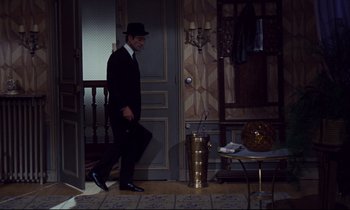 Movie still from “Le Grand Amour” (1969), directed by Pierre Étaix – A man in a suit and hat walking down the hall way; Wide shot, High angle