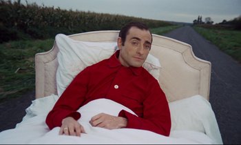 Movie still from “Le Grand Amour” (1969), directed by Pierre Étaix – A man laying in a bed wearing a red shirt; Medium shot, High angle