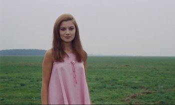 Movie still from “Le Grand Amour” (1969), directed by Pierre Étaix – A woman in a pink dress standing in a green field; Medium shot, Low angle