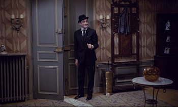 Movie still from “Le Grand Amour” (1969), directed by Pierre Étaix – A man in a suit and hat standing in front of a door; Medium shot, High angle
