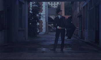 Movie still from “Le Grand Amour” (1969), directed by Pierre Étaix – A man holding an umbrella while standing on the sidewalk; Wide shot, Low angle