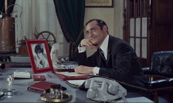 Movie still from “Le Grand Amour” (1969), directed by Pierre Étaix – A man sitting at a table with a picture of a woman; Medium shot, Over the shoulder angle