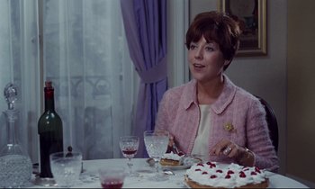 Movie still from “Le Grand Amour” (1969), directed by Pierre Étaix – A woman sitting at a table with a piece of cake on top of it; Medium shot, Over the shoulder angle