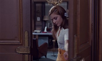 Movie still from “Le Grand Amour” (1969), directed by Pierre Étaix – A woman standing in front of an open door in a room; Medium shot, Low angle