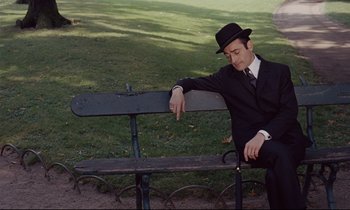 Movie still from “Le Grand Amour” (1969), directed by Pierre Étaix – A man sitting on top of a wooden park bench; Medium shot, High angle