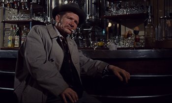 Movie still from “Le Grand Amour” (1969), directed by Pierre Étaix – A man sitting in front of a bar wearing a hat; Medium shot, Low angle