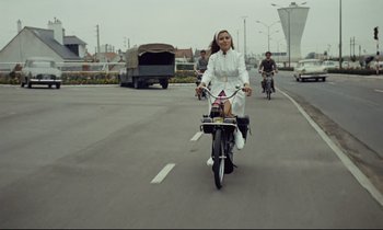 Movie still from “Le Grand Amour” (1969), directed by Pierre Étaix – A woman is riding a bike down the street; Wide shot, Low angle