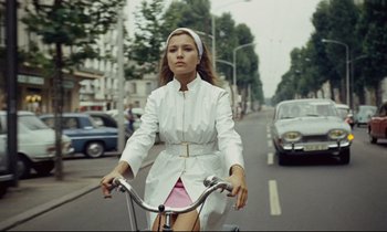 Movie still from “Le Grand Amour” (1969), directed by Pierre Étaix – A woman riding a bike down a street; Medium shot, Low angle
